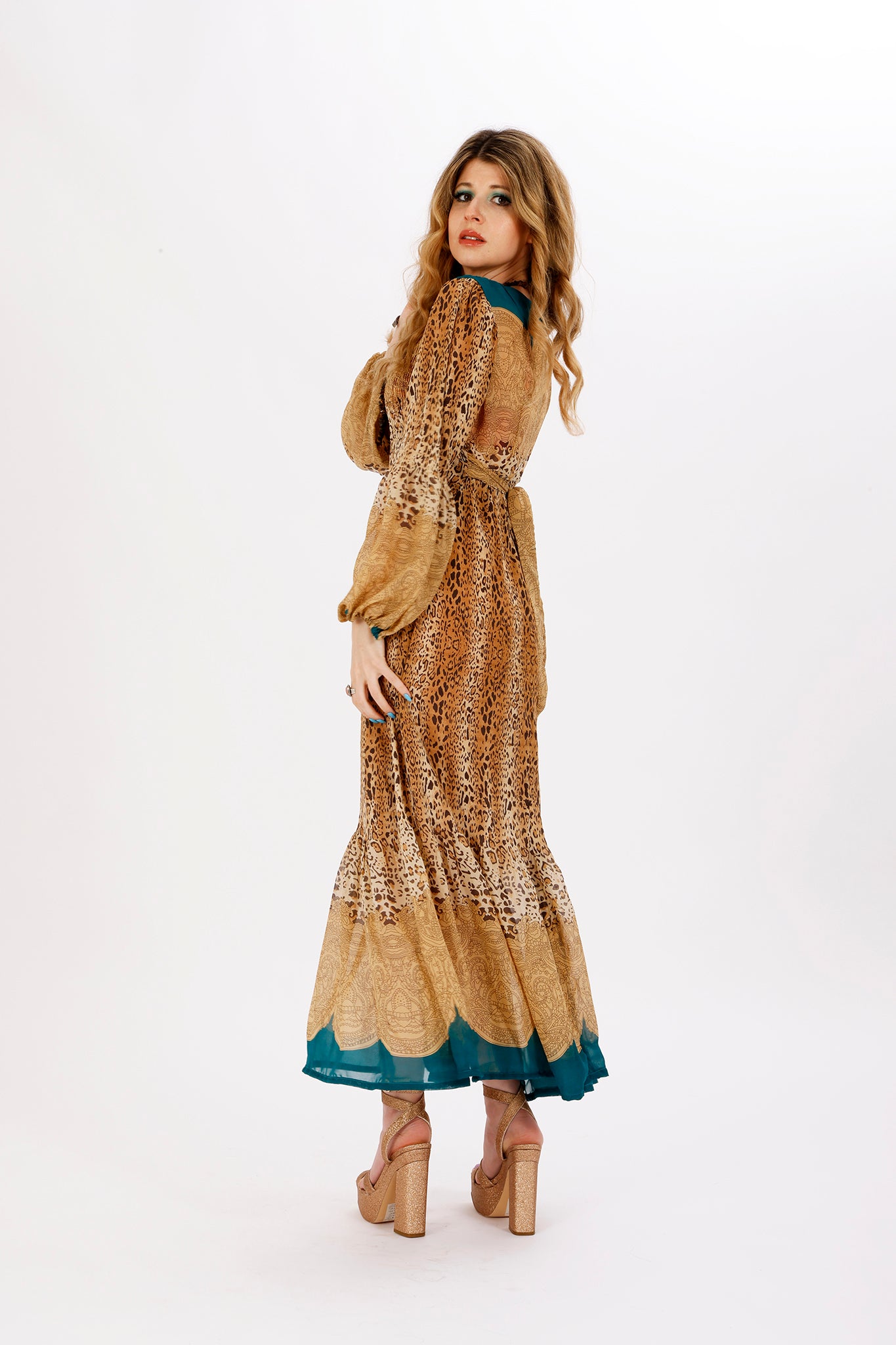A woman standing and posing in a leopard print maxi dress with balloon puff sleeves and an empire waistline.