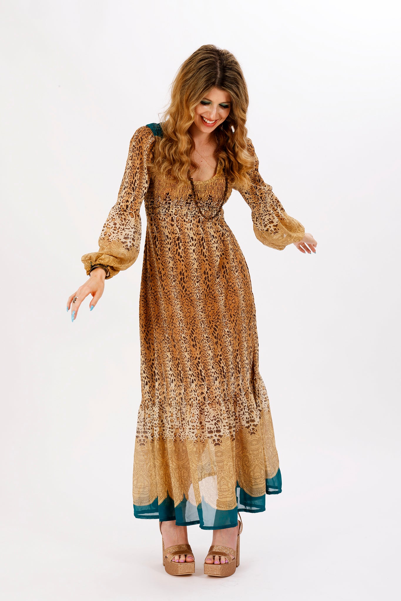 A woman standing and posing in a leopard print maxi dress with balloon puff sleeves and an empire waistline.